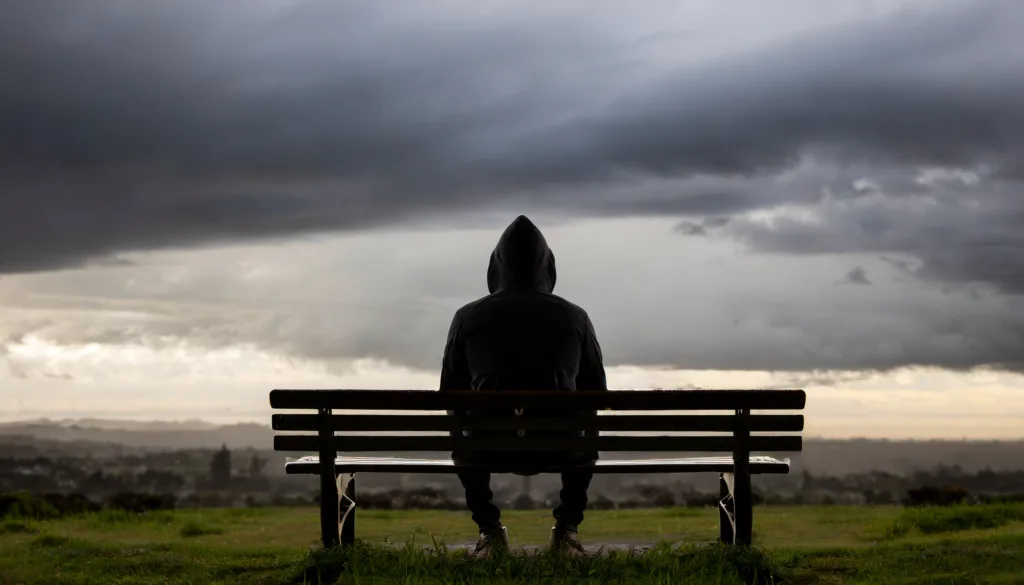 Depressed man in hoodie sitting on a bench. Depression.