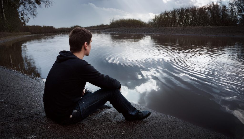 Youth sitting at the edge of a river bank.