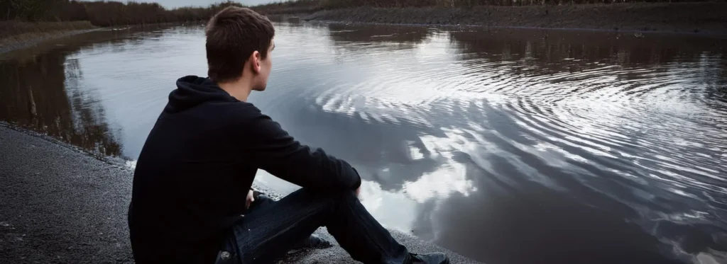 Man looks at lake reflecting on addiction
